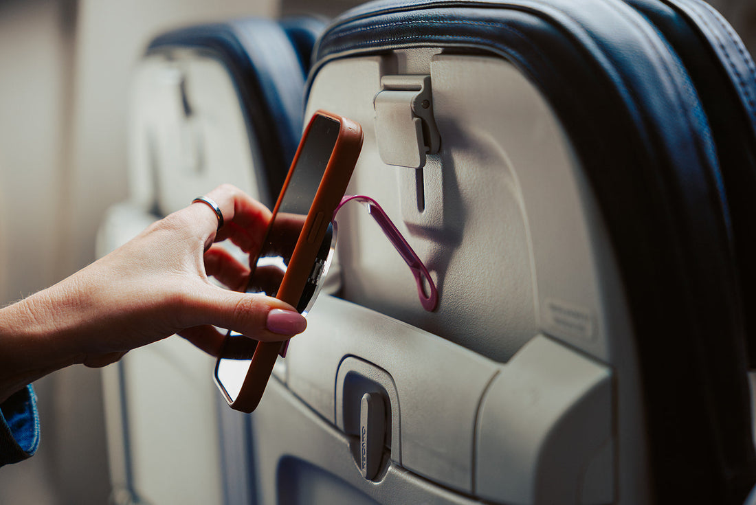 A traveler hanging their phone on an airplane seat using the Mo' Bettah MagSafe Airplane Phone Holder