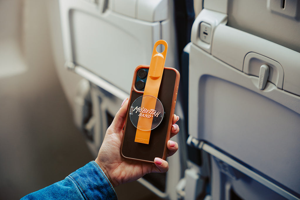 Traveler showing a orange Mo'bettah Airplane Phone Holder on a MagSafe compatible iPhone