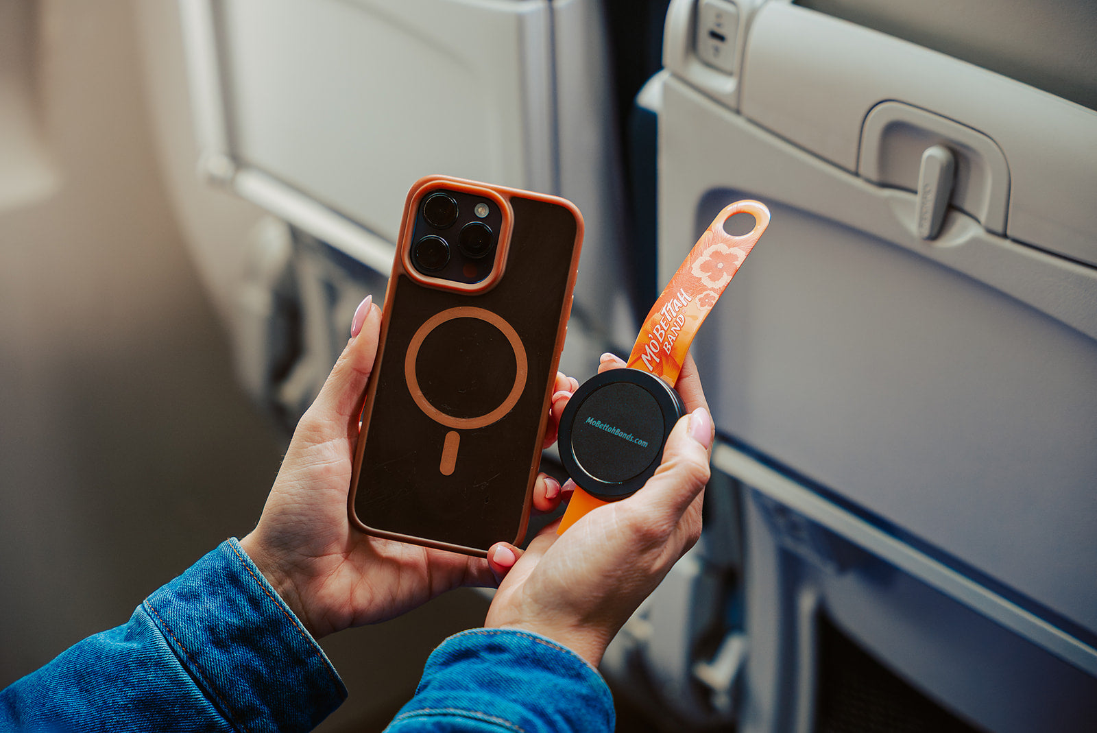 Traveler holding a orange Mo'bettah Airplane Phone Holder next to a MagSafe compatible iPhone before attaching it