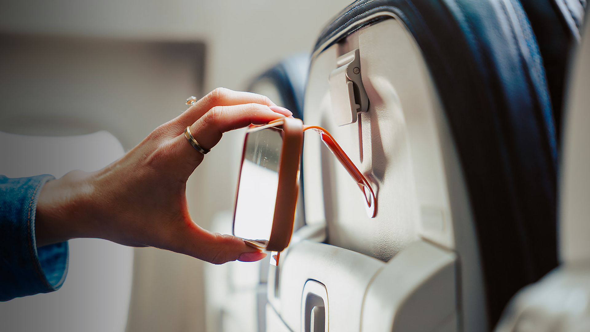 Attaching the orange Mo'bettah Airplane Phone Holder to an airplane seat pocket for hands-free viewing