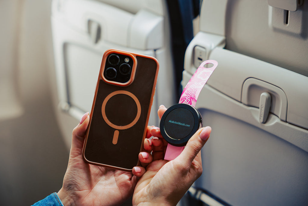 Traveler holding a pink Mo'bettah Airplane Phone Holder next to a MagSafe compatible iPhone before attaching it